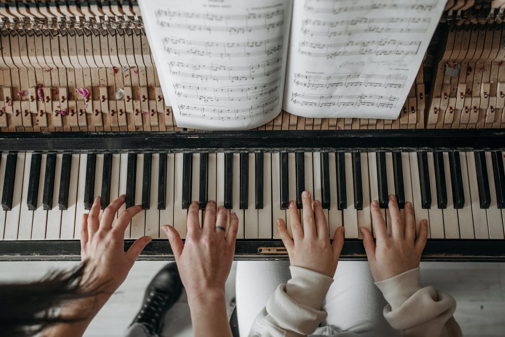 A music teacher's hands and a student's hands playing the piano