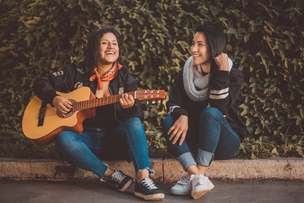 2 people sat together playing a guitar and singing